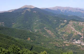 Forested ridges and the rounded summit of Pelister above Armensko, a hairpin road cut into the slope on the right